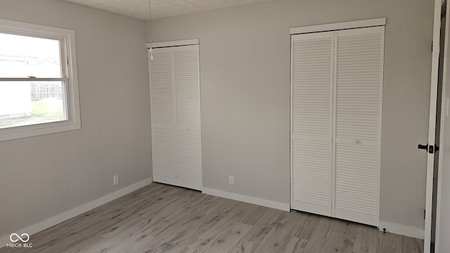 unfurnished bedroom featuring two closets, light hardwood / wood-style flooring, and a textured ceiling