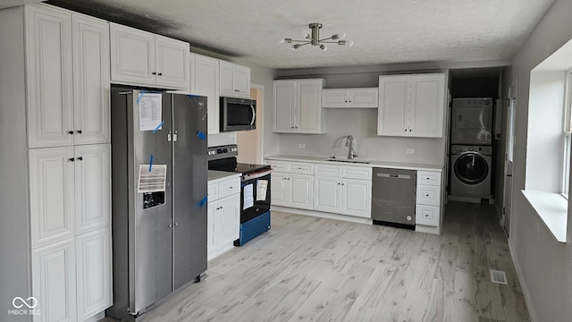 kitchen featuring stainless steel appliances, white cabinetry, stacked washer / drying machine, and sink