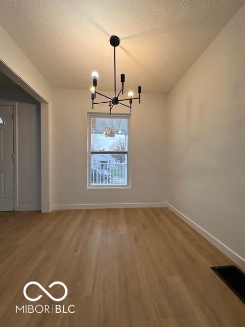 unfurnished dining area with wood-type flooring, a textured ceiling, and an inviting chandelier