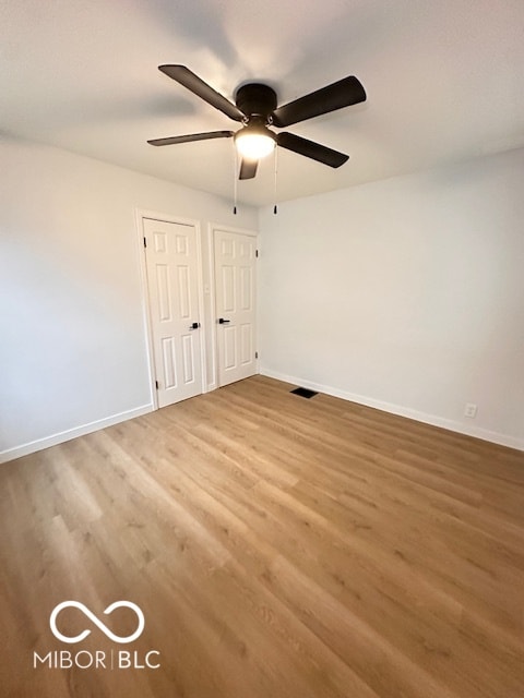 unfurnished bedroom featuring wood-type flooring, ceiling fan, and multiple closets