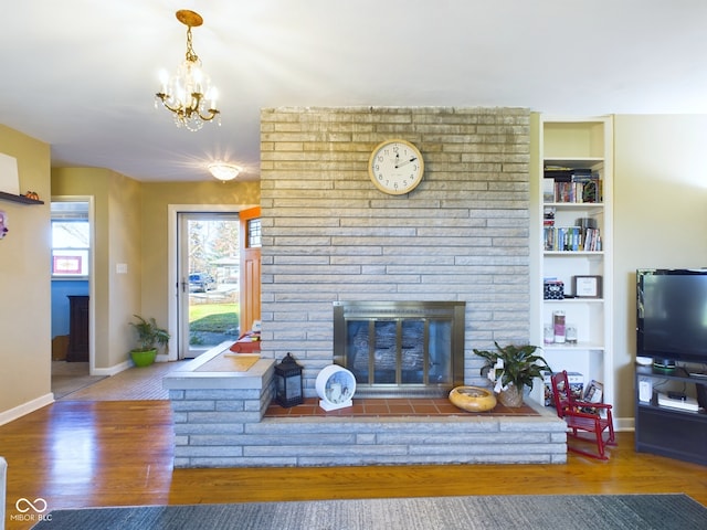 living room with hardwood / wood-style floors, an inviting chandelier, built in features, and a brick fireplace