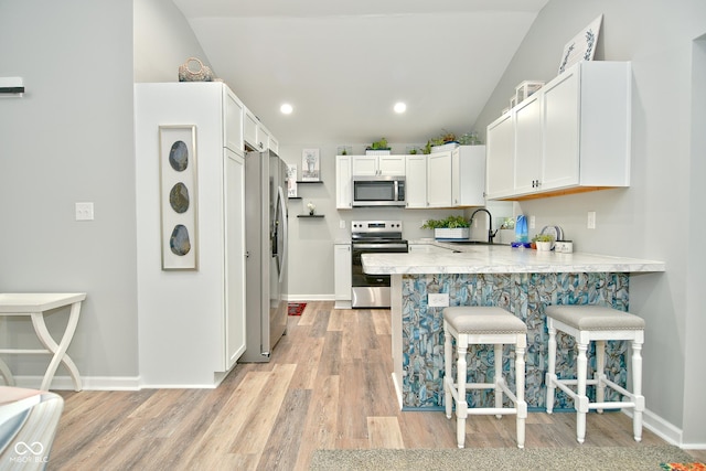 kitchen featuring sink, a kitchen breakfast bar, lofted ceiling, white cabinets, and appliances with stainless steel finishes