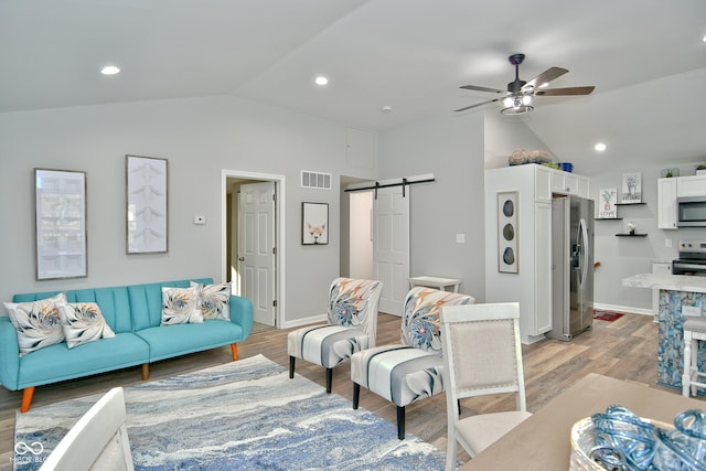 living room featuring lofted ceiling, a barn door, light wood-type flooring, and ceiling fan