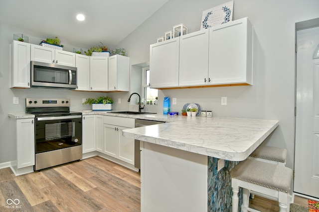 kitchen featuring a breakfast bar, lofted ceiling, sink, kitchen peninsula, and stainless steel appliances