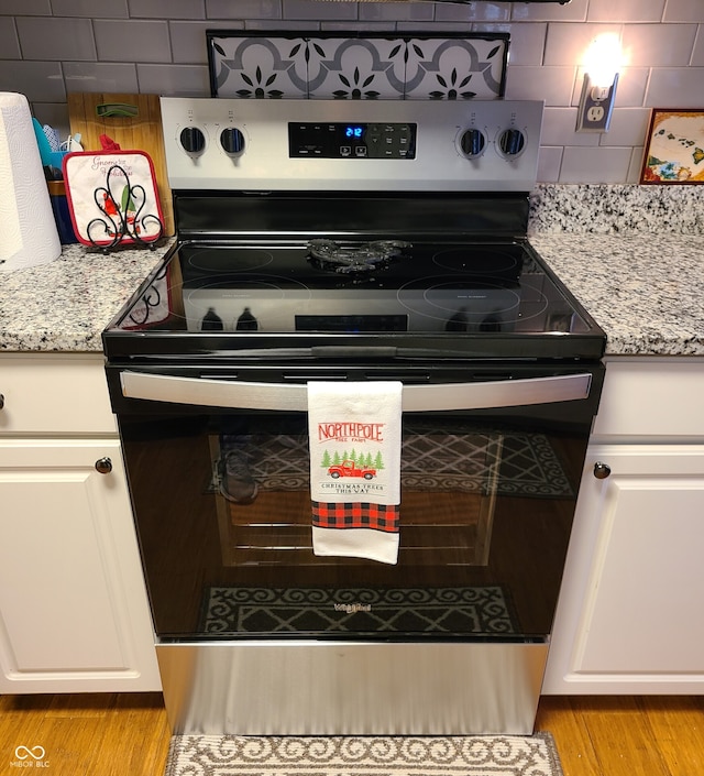 kitchen with light stone countertops, decorative backsplash, white cabinetry, light hardwood / wood-style floors, and stainless steel electric range oven