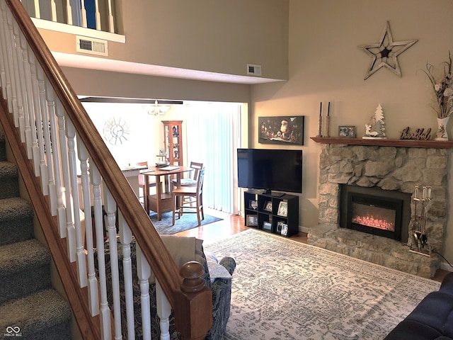 living room with a chandelier, a towering ceiling, hardwood / wood-style flooring, and a stone fireplace