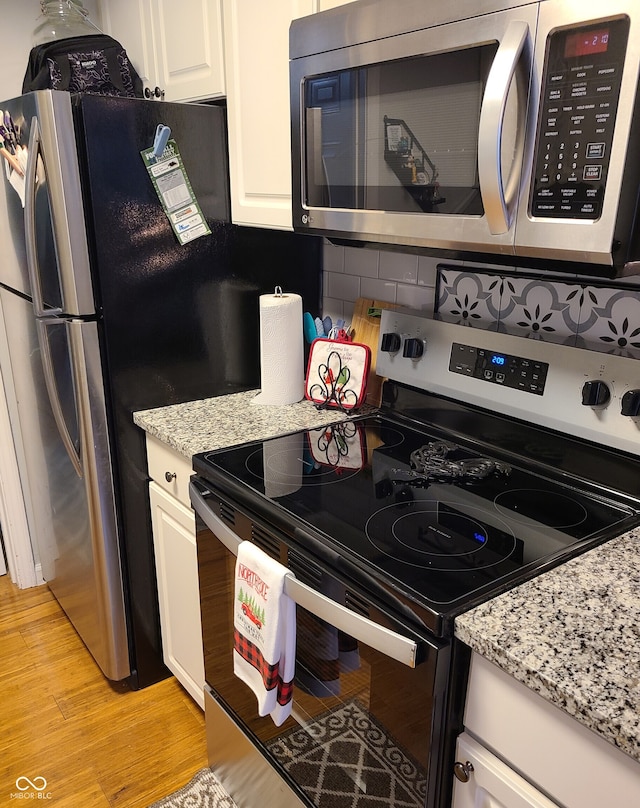 kitchen with white cabinets, appliances with stainless steel finishes, light wood-type flooring, and light stone countertops