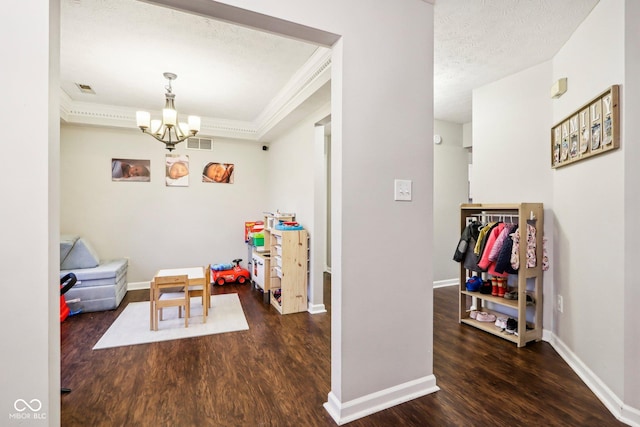 recreation room featuring dark wood-type flooring, ornamental molding, a textured ceiling, and a notable chandelier