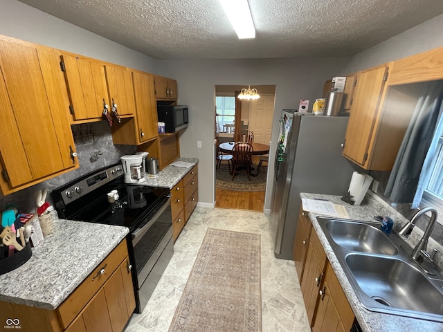 kitchen featuring sink, backsplash, a chandelier, a textured ceiling, and appliances with stainless steel finishes