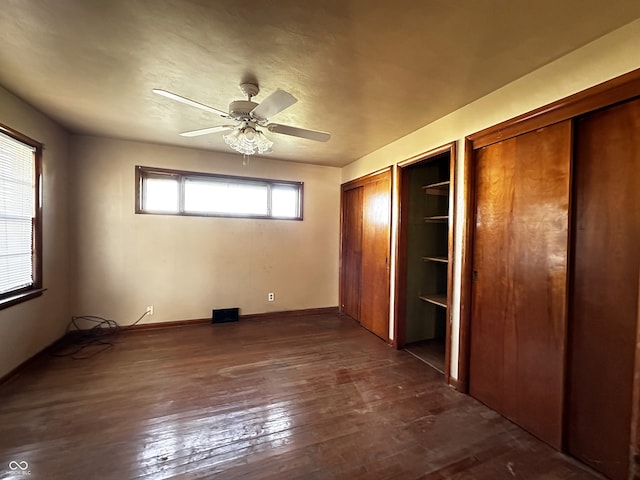 unfurnished bedroom featuring ceiling fan, dark hardwood / wood-style floors, and multiple closets