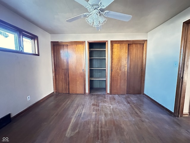 unfurnished bedroom featuring ceiling fan, dark hardwood / wood-style floors, and multiple closets