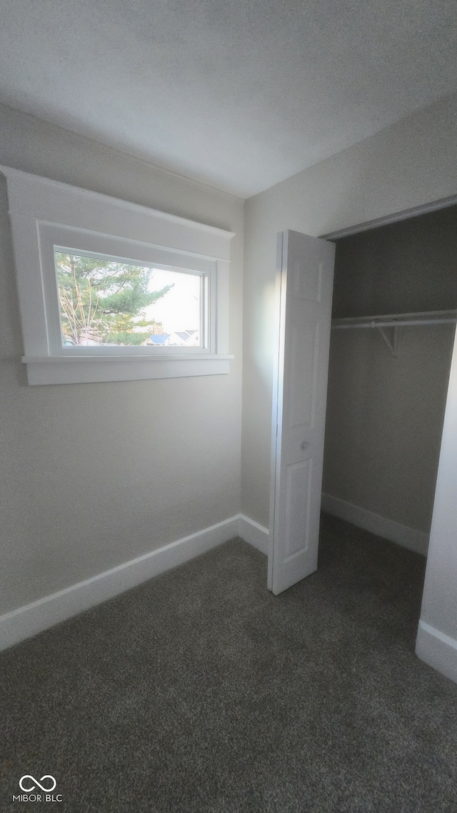 unfurnished bedroom with dark carpet and a closet