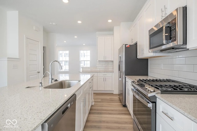 kitchen featuring light stone countertops, appliances with stainless steel finishes, sink, white cabinets, and light hardwood / wood-style floors