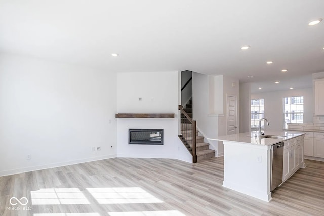 kitchen with stainless steel dishwasher, sink, a center island with sink, light hardwood / wood-style floors, and white cabinetry