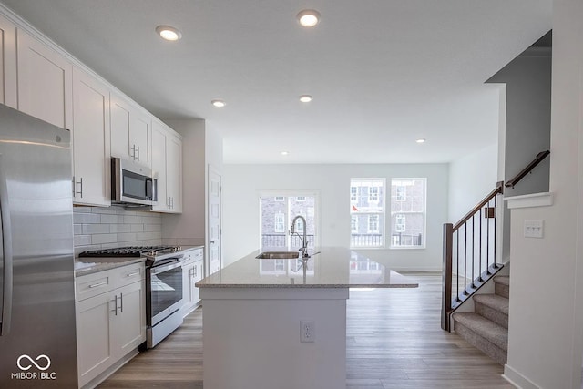 kitchen with stainless steel appliances, sink, white cabinets, light hardwood / wood-style floors, and an island with sink