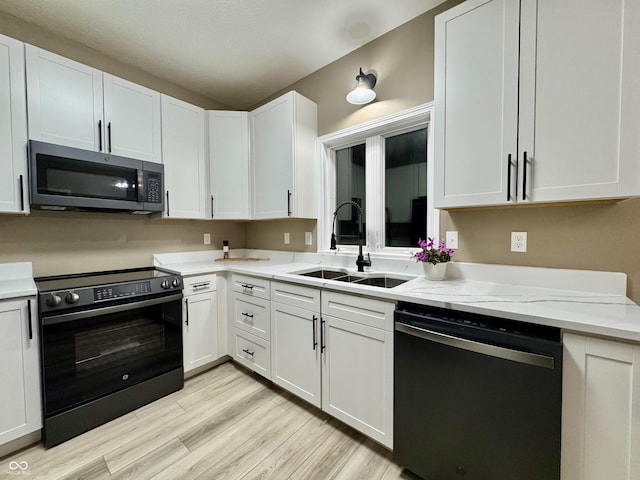 kitchen featuring black appliances, sink, light stone countertops, light hardwood / wood-style floors, and white cabinetry