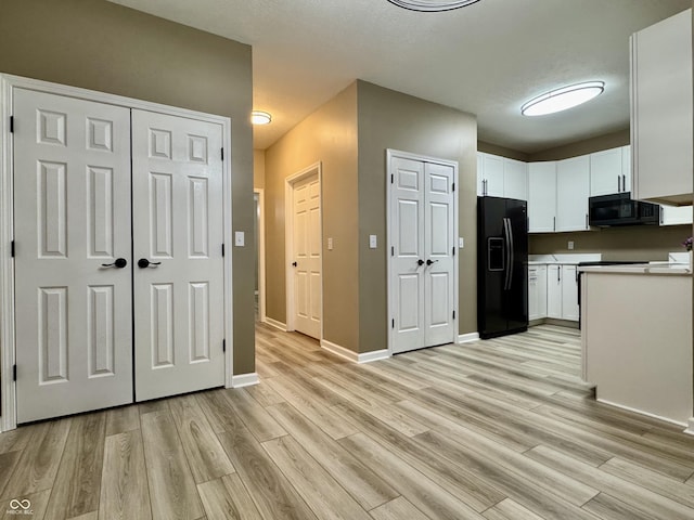 kitchen with white cabinets, a textured ceiling, light wood-type flooring, and black appliances