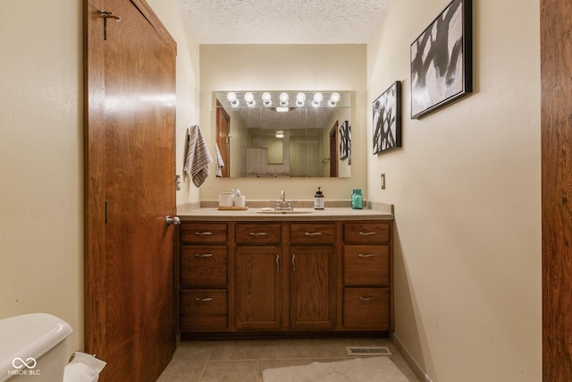 bathroom featuring tile patterned flooring, vanity, a textured ceiling, and toilet