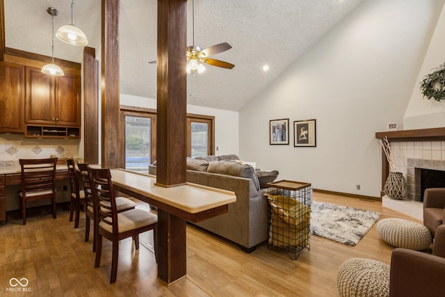 living room with high vaulted ceiling, a tile fireplace, and light hardwood / wood-style flooring