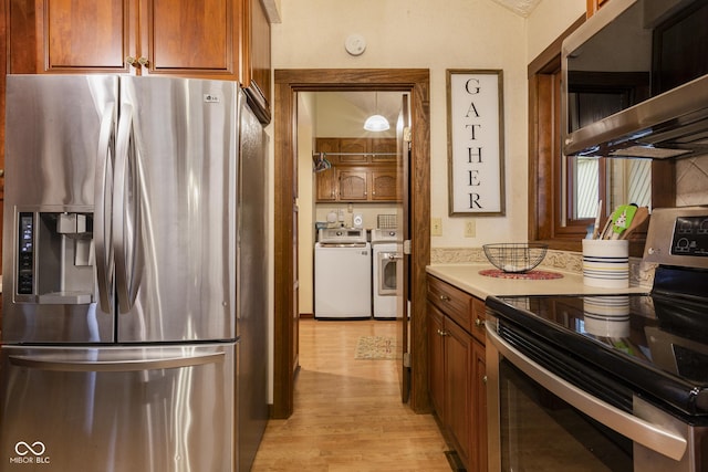 kitchen with washing machine and clothes dryer, hanging light fixtures, light wood-type flooring, and appliances with stainless steel finishes