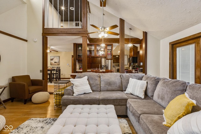 living room with a textured ceiling, light hardwood / wood-style floors, high vaulted ceiling, and ceiling fan