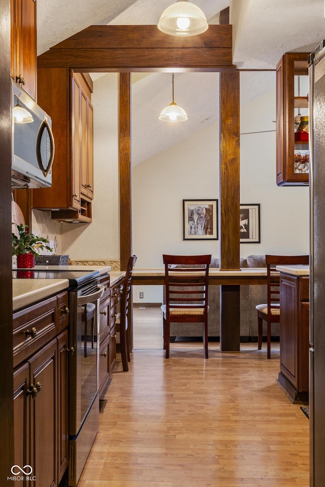 kitchen with stove, pendant lighting, light hardwood / wood-style floors, and lofted ceiling