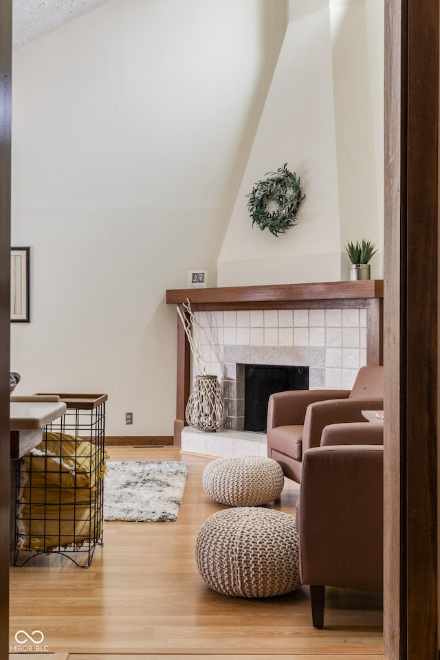 living room featuring hardwood / wood-style flooring, a tile fireplace, and vaulted ceiling