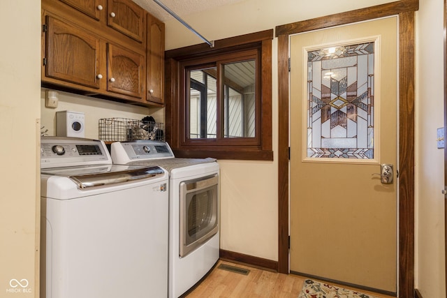 clothes washing area with separate washer and dryer, cabinets, and light hardwood / wood-style floors