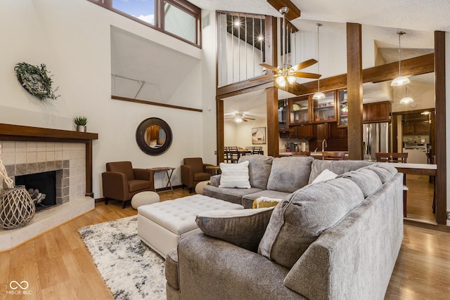 living room featuring ceiling fan, sink, high vaulted ceiling, hardwood / wood-style floors, and a tiled fireplace