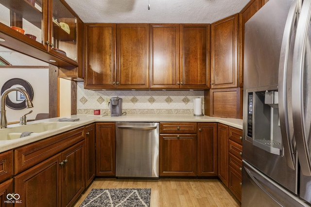 kitchen with backsplash, sink, light wood-type flooring, a textured ceiling, and appliances with stainless steel finishes