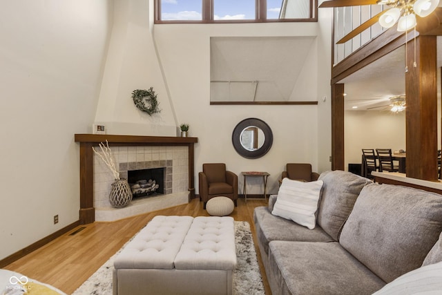 living room with ceiling fan, a tile fireplace, wood-type flooring, and a high ceiling