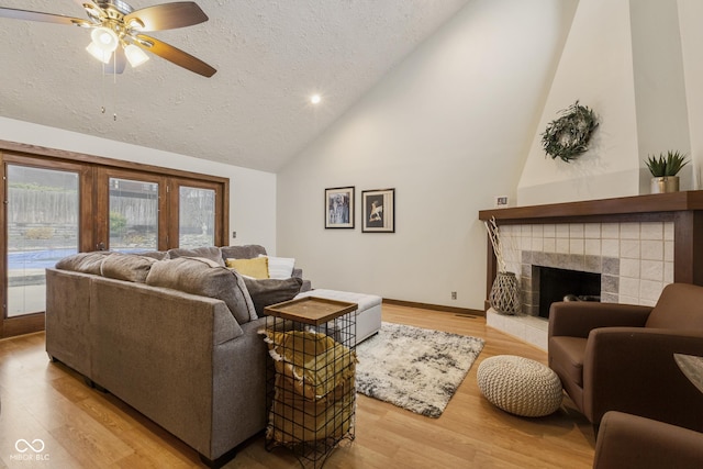 living room featuring ceiling fan, light hardwood / wood-style flooring, a tile fireplace, and vaulted ceiling