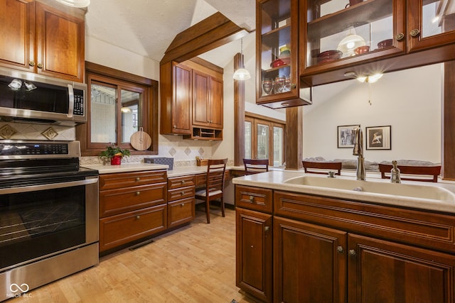 kitchen with light wood-type flooring, tasteful backsplash, stainless steel appliances, sink, and pendant lighting