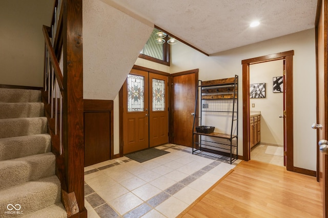 foyer entrance with vaulted ceiling, a textured ceiling, and light hardwood / wood-style flooring