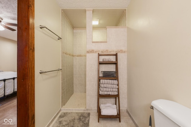 bathroom featuring tile patterned floors, ceiling fan, toilet, tiled shower, and a textured ceiling