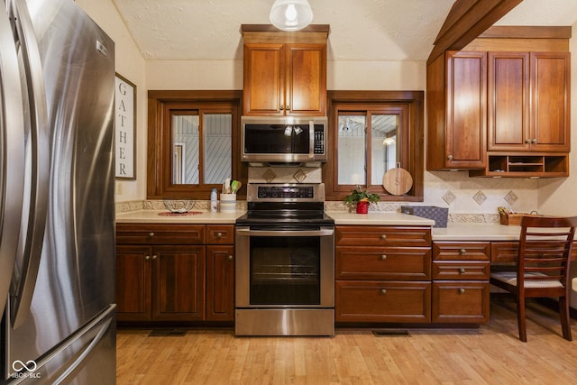 kitchen with backsplash, light hardwood / wood-style floors, a textured ceiling, and appliances with stainless steel finishes