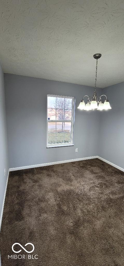 spare room featuring carpet, a textured ceiling, and a notable chandelier