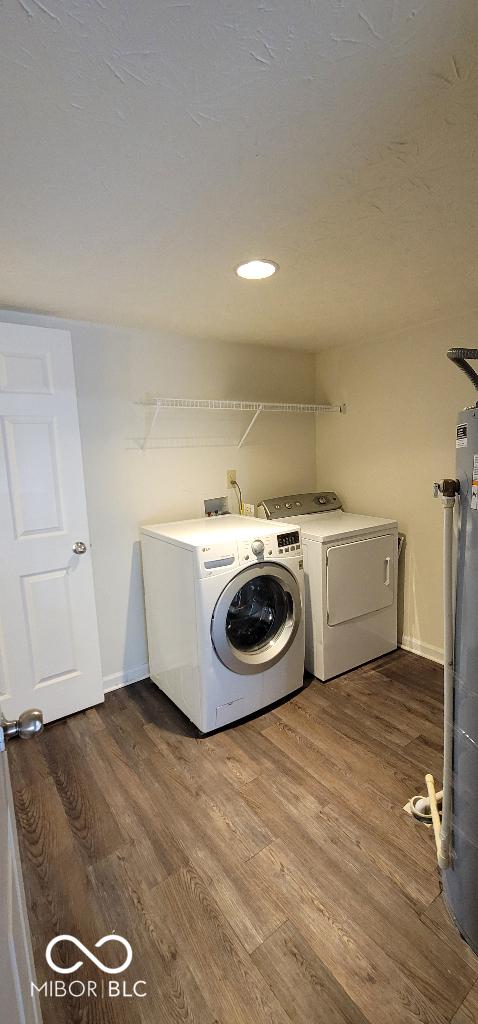 clothes washing area with wood-type flooring, water heater, and washing machine and clothes dryer