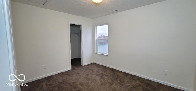 unfurnished bedroom with a walk in closet, a closet, and dark carpet