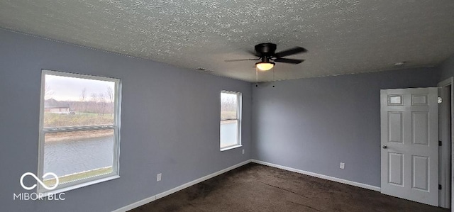 spare room featuring dark colored carpet, a textured ceiling, a wealth of natural light, and ceiling fan