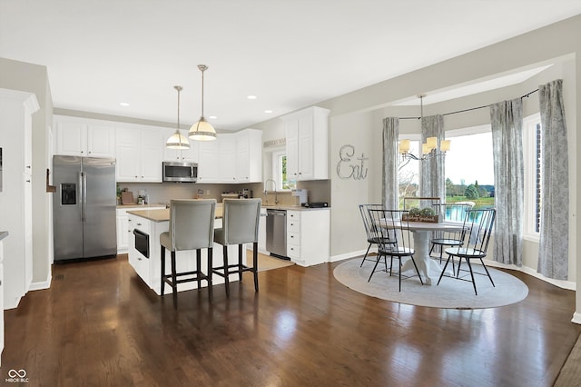 kitchen featuring white cabinets, decorative light fixtures, a kitchen island, and stainless steel appliances