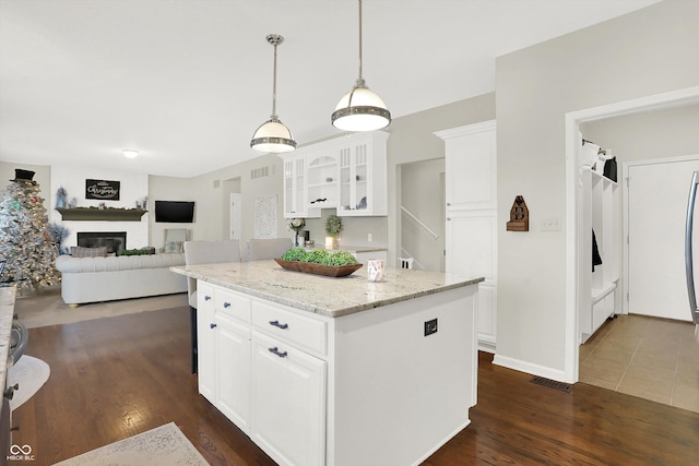 kitchen featuring light stone countertops, a center island, dark hardwood / wood-style flooring, pendant lighting, and white cabinets