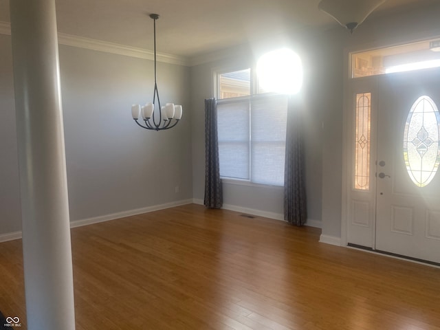 entryway with hardwood / wood-style floors, crown molding, a wealth of natural light, and an inviting chandelier