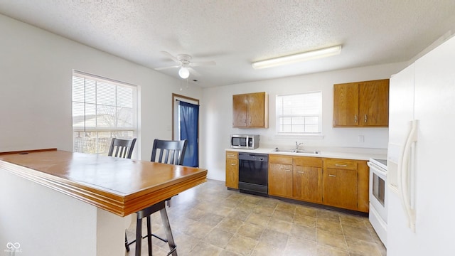 kitchen featuring a kitchen bar, a textured ceiling, white appliances, ceiling fan, and sink