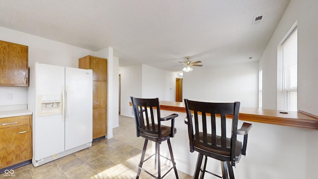 kitchen with a kitchen breakfast bar, ceiling fan, and white refrigerator with ice dispenser