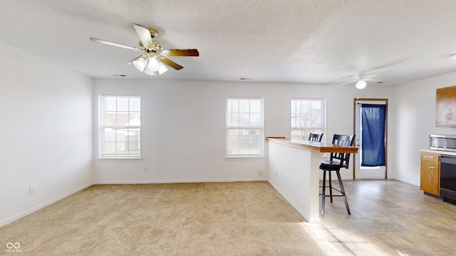 kitchen with a kitchen breakfast bar, ceiling fan, light colored carpet, and a textured ceiling