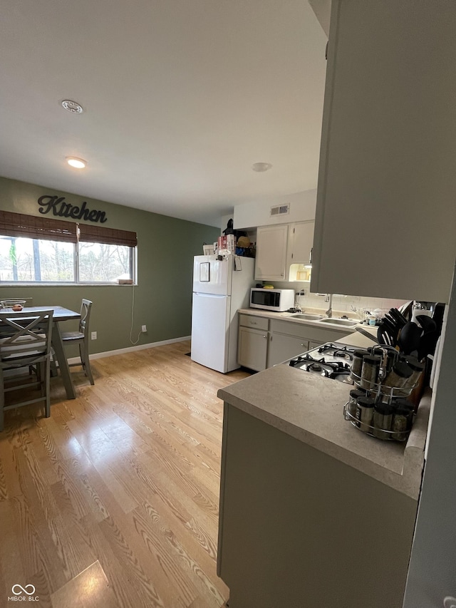 kitchen with white cabinets, light wood-type flooring, white appliances, and sink