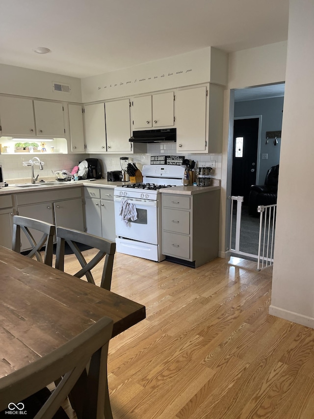 kitchen featuring light wood-type flooring, tasteful backsplash, white range with gas cooktop, and sink