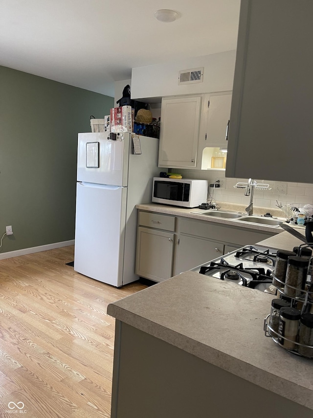 kitchen with tasteful backsplash, sink, white appliances, and light hardwood / wood-style flooring