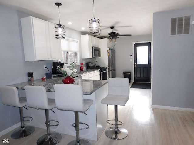 kitchen with white cabinetry, kitchen peninsula, light hardwood / wood-style floors, a breakfast bar area, and appliances with stainless steel finishes